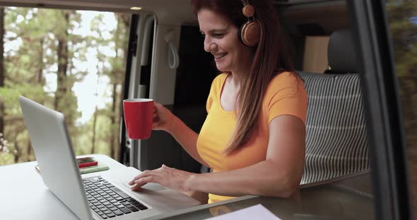 Senior caucasian woman using laptop and wireless headphone inside mini van camper
