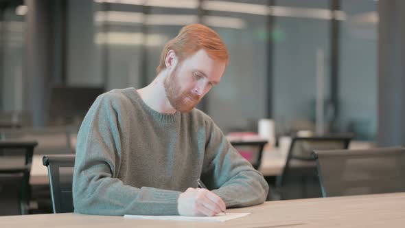 Young Man Thinking While Writing on Paper in Office