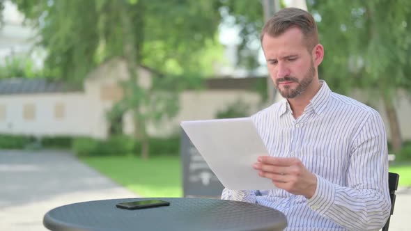 Middle Aged Man Reading Documents in Outdoor Cafe