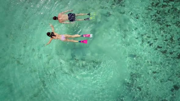 Aerial view of man and woman swimming in masks and flippers in turquoise water.