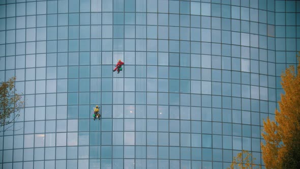 Two Men Workers Cleaning the Exterior Windows of a Skyscraper - Industrial Alpinism - Hanging on