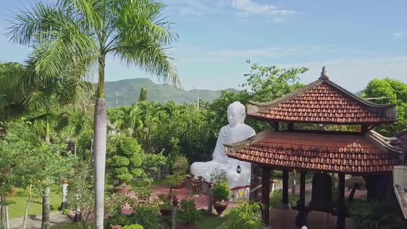Flycam Moves To Buddha Sculpture Among Plants Buildings alt