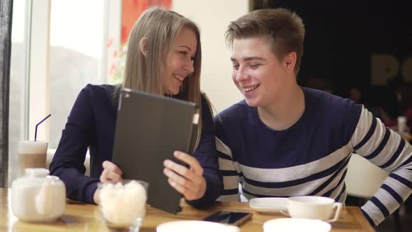 Young Couple Sitting in Cafe Using Digital Tablet Watching Movies and Shopping