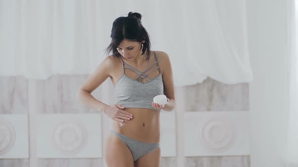 Young Beautiful Woman Applying Moisturizer Cream on Her Belly at Home