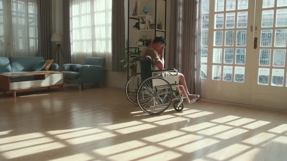 Disappointed Young Asian Boy Sitting In A Wheelchair Near Door In The House