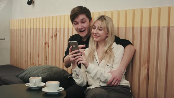 Happy Couple Using Smartphone Together and Laughing in Cafe