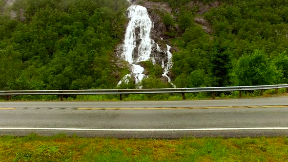 A Beautiful Powerful Waterfall Flows From a High Mountain Under the Bridge and Flows Into a Large