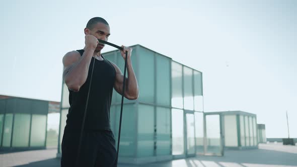 Bald serious sportsman wearing black T-shirt doing sport exercises with an elastic band