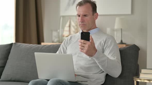 Attractive Middle Aged Businessman Using Smartphone on Sofa 