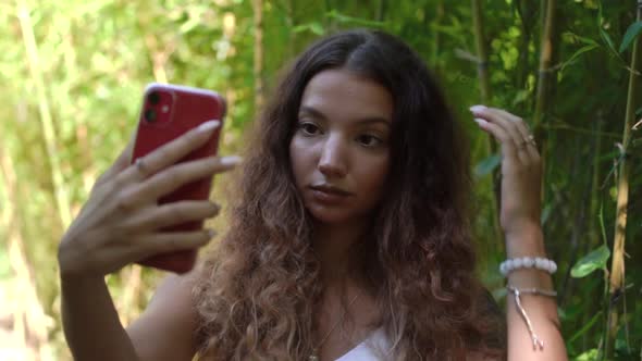 Elegant Lady Makes Selfie Holding Red Smartphone in Park