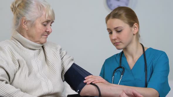 Young Nurse Measuring Disabled Elderly Female Blood Pressure and Taking Records