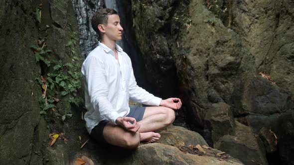 Handsome Young Man Meditates on Rock in Yoga Lotus Position