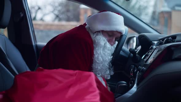 Side View Exhausted Father Christmas Sleeping in Car Yawning Leaning on Steering Wheel
