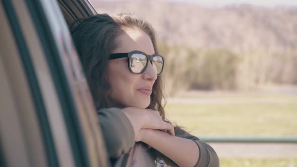 Girl in Sunglasses Sits By Car Window Smiles and Waves Hand