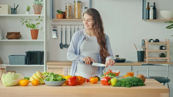 Happy Pregnant Woman Enjoying Preparing a Salad Cutting Organic Vegetables