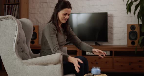 Young Woman Sitting on the Armchair Lights a Candle and Meditates