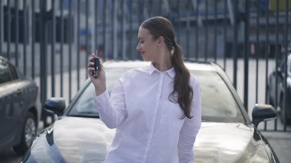 Happy Young Successful Caucasian Woman Bragging Car Key Standing at New Luxurious Black Vehicle in