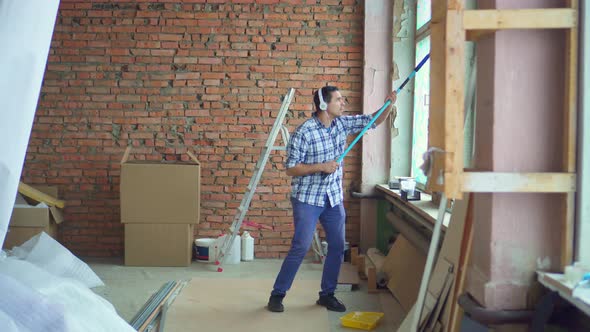 an Energetic and Contented Man in a Shirt Paints the Walls During an Apartment Renovation