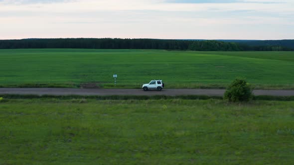 Aerial View of a Car Driving in Nature on a Field at Sunset