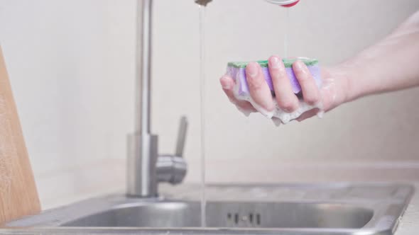 Hand Pours Liquid Detergent Onto a Sponge and Starts Washing Dishes Closeup