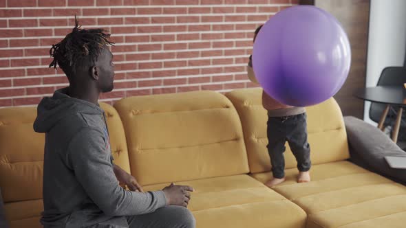 AfricanAmerican Father Playing with Cute Little Boy on Sofa in Cozy Home Interior