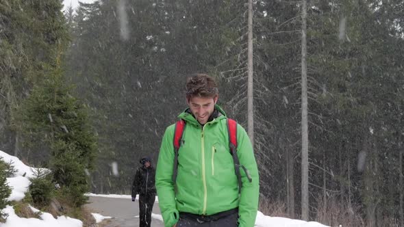 A man and woman couple hiking while it is snowing in mountains in the winter.