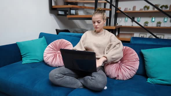 Wide Shot Absorbed Teenage Caucasian Girl Surfing Internet on Laptop Sitting in Living Room at Home