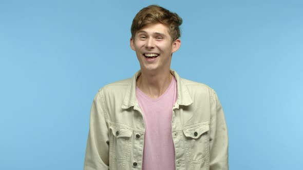 Handsome Young Man Standing Over Blue Background and Laughing at Something Funny Chuckle Over