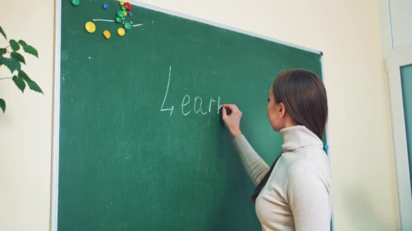 Young English teacher is writing on the board. Beautiful woman in sweater writes the english words