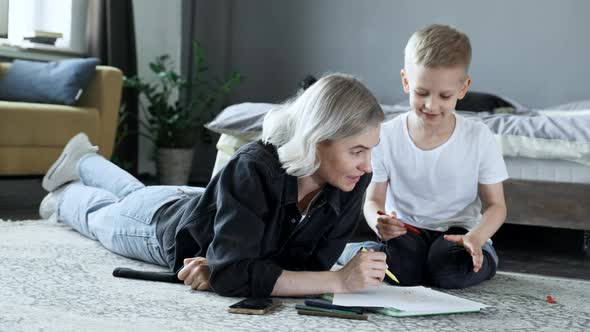 A Young Mother and a Boy Child Are lying on the Floor, Drawing with Felt-Tip Pens on Paper