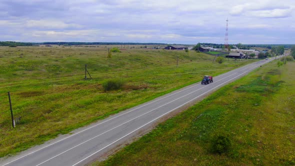 A Tractor is Driving on a Road with a Trailer for Packing Haystacks