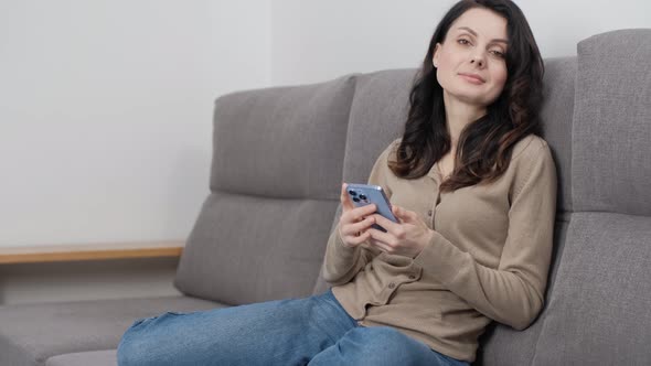Happy woman with smart phone posing on couch at home