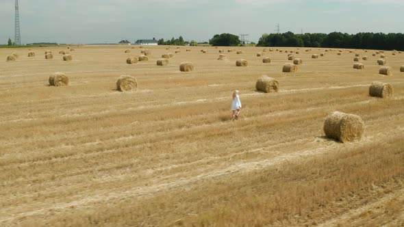 Beautiful young girl in a white shirt on a field among sheaves of hay. Aerial view	