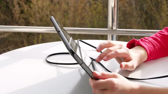 Close-up of Hands, Teenager Girl Typing, Working on Tablet, on Open Balcony. Spring Sunny Day.