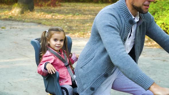 Father riding bicycle with daughter sitting in child seat
