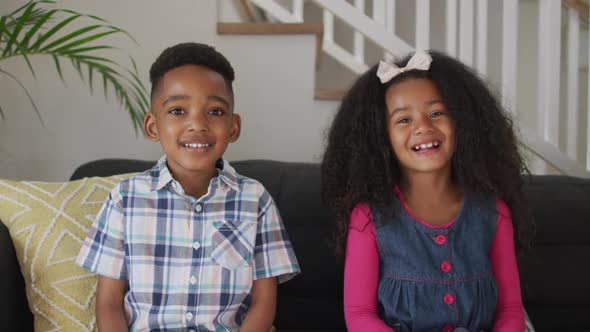 African american siblings siting on sofa, looking at camera and smiling