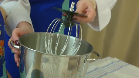 A Woman in a Cooks Uniform Removes the Bowl of Cream From the Kitchen Machine and Hits the Whisk on