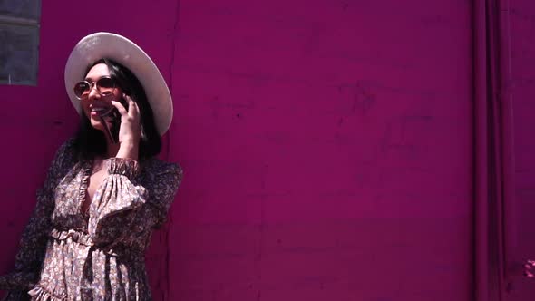 Young Smiling Woman Talking on Smartphone By Purple Pink Wall on Hot Sunny Day