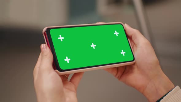 Close-up hands holding a horizontal green screen phone on transport.