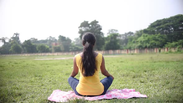 Young Asian girl doing meditation and Indian pranayam yoga showing back at morning sunrise