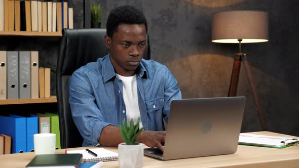 African American Businessman Works for Laptop Turns to Camera and Smiles