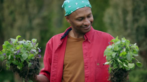 Happy Smiling Young African American Man Holding Flowers for Transplanting in Hands Standing in