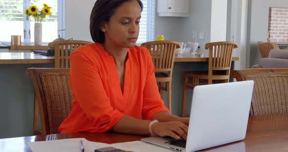 Front view of mixed race mature woman working on laptop on desk at home 4k