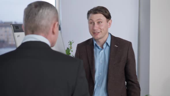 Cheerful Confident Businessman Patting Shoulder and Talking to Senior Partner in Office