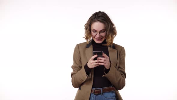 Portrait of Happy European Woman Wearing Casual Clothing Brown Jacket and Jeans Holding Smartphone