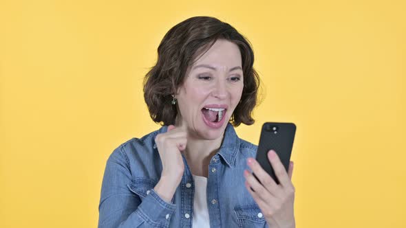 Old Woman Celebrating on Smartphone, Yellow Background 