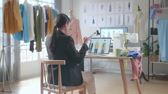 Back View Of Asian Female Designer In Business Suit Celebrating While Designing Clothes On A Laptop