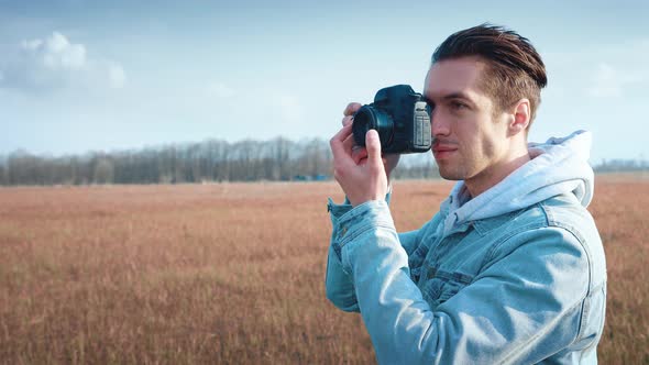 Young Male Photographer Taking Photo on Professional Photocamera Standing at Red Field