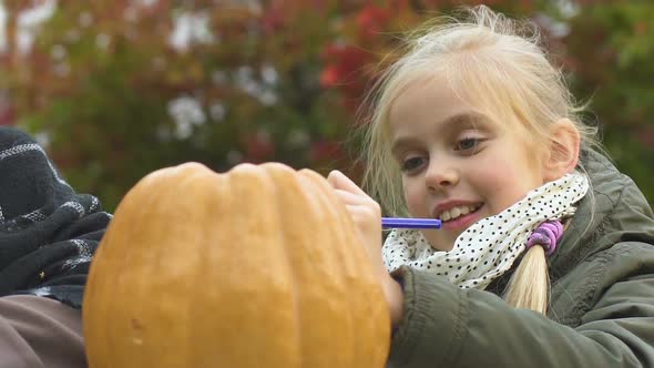 Little Girl Drawing on Pumpkin, Mother Smiling, Halloween Party Preparation