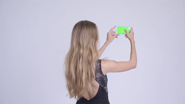 Rear View of Happy Young Blonde Woman Taking Picture with Phone Ready for Vacation